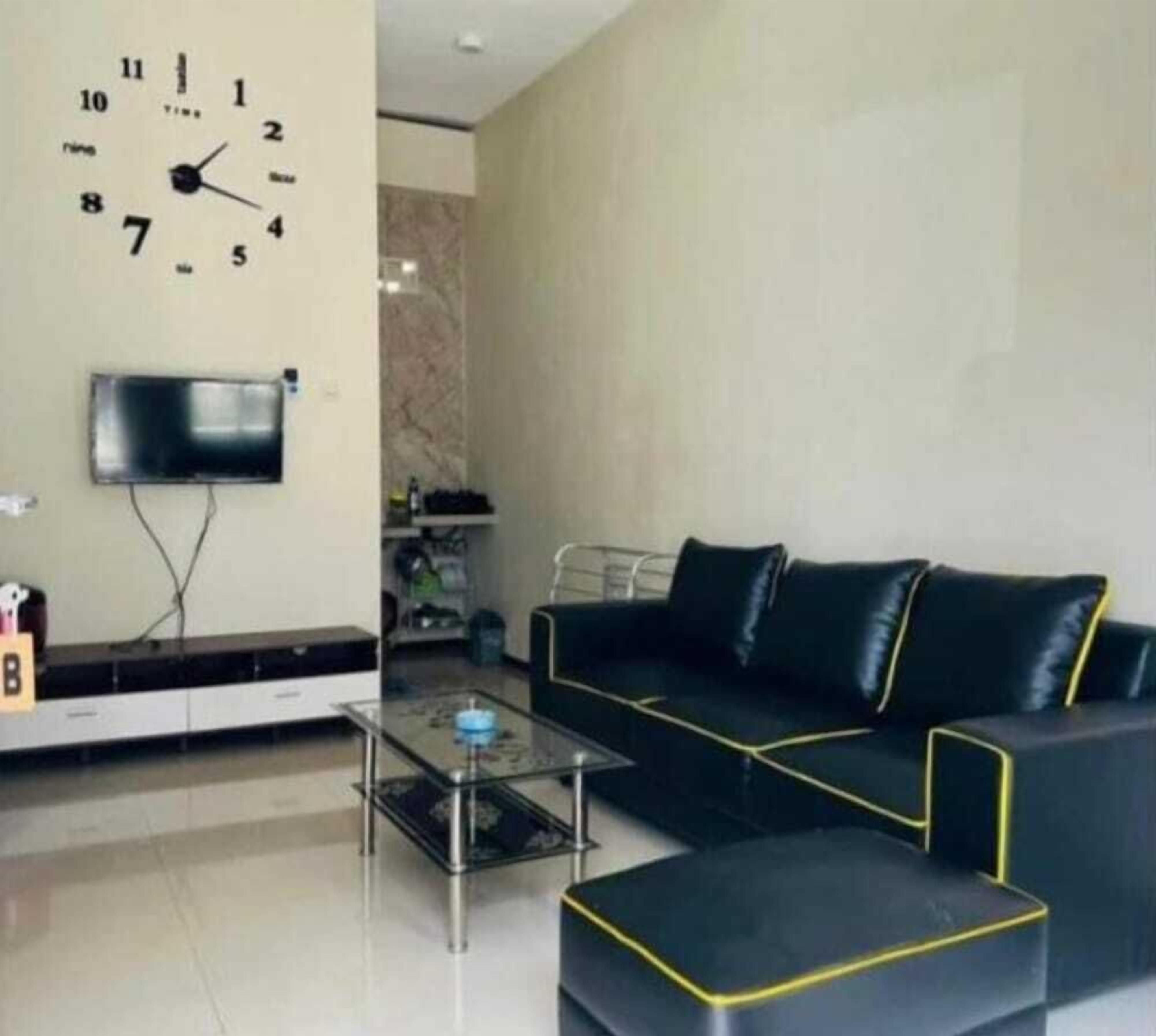 A modern living room with a black sofa, a glass coffee table, and a wall clock.