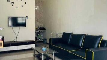 A modern living room with a black sofa, a glass coffee table, and a wall clock.