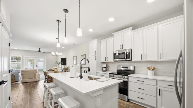 A modern kitchen with white cabinetry, a central island with stools, stainless steel appliances, and a wooden floor. - 5-Min Walk to Beach | Good Morning Rentals (Jacksonville Beach)