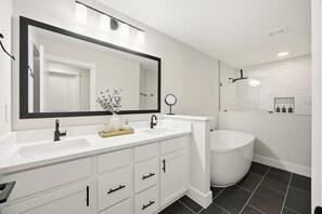 A modern bathroom with a white vanity, a large mirror, a round mirror, a bathtub, and a toilet. - 5-Min Walk to Beach | Good Morning Rentals (Jacksonville Beach)