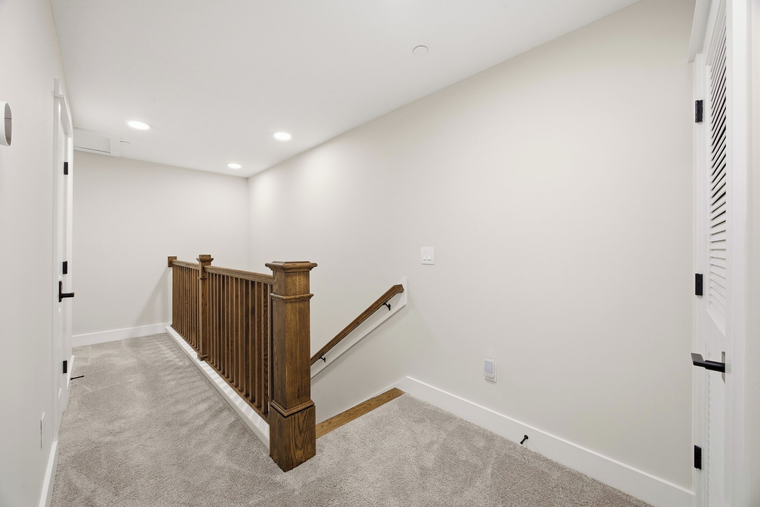 Un couloir propre, aux murs blancs, avec un escalier en bois et un plancher recouvert de moquette.