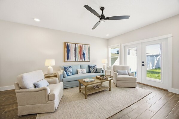 A living room with a sofa, armchairs, a coffee table, and a ceiling fan. - 5-Min Walk to Beach | Good Morning Rentals (Jacksonville Beach)