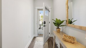 A hallway with a white door, a mirror, a plant, and a woven basket on a wooden console. - 5-Min Walk to Beach | Good Morning Rentals (Jacksonville Beach)