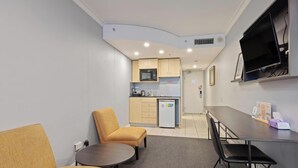 Habitación de hotel pequeña con kitchenette, un sofá, una mesita redonda y un televisor montado en la pared.
