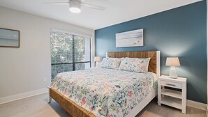 Ein Schlafzimmer mit einem Bett, einem Nachttisch, einem Deckenventilator und einem Fenster mit Jalousien.