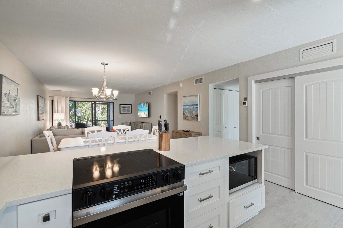 A modern kitchen with a built-in stove, white cabinetry, and a dining area with a white table and chairs.