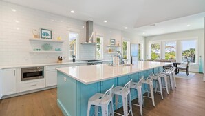 Una cocina moderna con armarios blancos, una isla grande con taburetes y vistas al exterior a través de amplios ventanales.