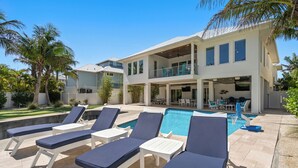 Una casa moderna con piscina, sillas de descanso y un patio cubierto.
