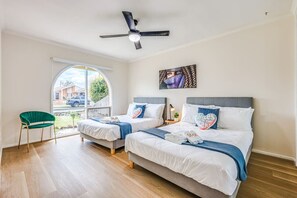 Ett hotellrum med två sängar, en takfläkt, ett stort fönster och en grön stol.