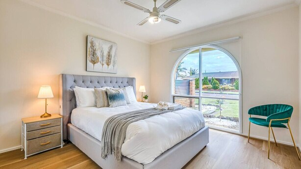 A bedroom with a large bed, a nightstand with a lamp, a ceiling fan, and a view through a large window. - StayAU Pet-Friendly 7Bed Spacious Retreat Morwell (Morwell)