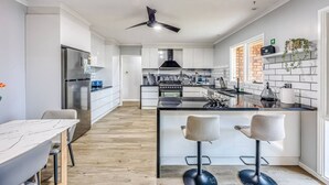 A modern kitchen with white cabinetry, a central island with bar stools, a built-in oven, and a stainless steel refrigerator. - StayAU Pet-Friendly 7Bed Spacious Retreat Morwell (Morwell)