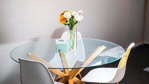 A round glass table with a white vase containing flowers, surrounded by white chairs with wooden legs.