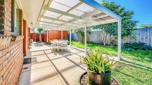 An outdoor patio with a covered seating area, a brick wall, and a wooden fence in the background.