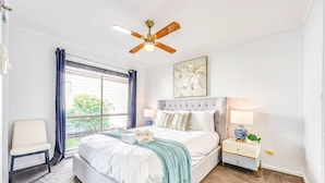 A bedroom with a bed, a chair, a nightstand, a lamp, a ceiling fan, and a window with curtains.