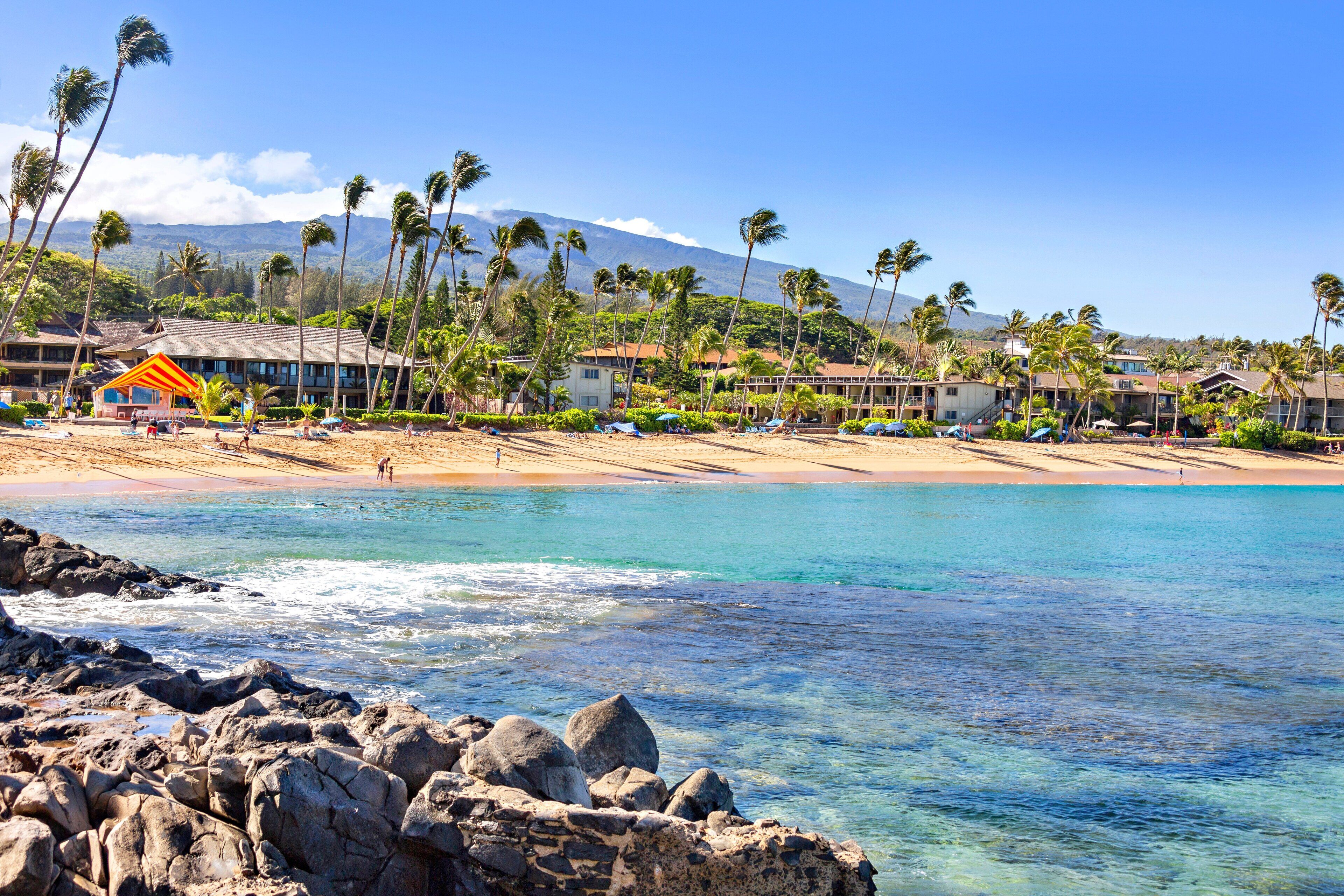 A beach resort with clear turquoise water, rocky shoreline, and palm trees.