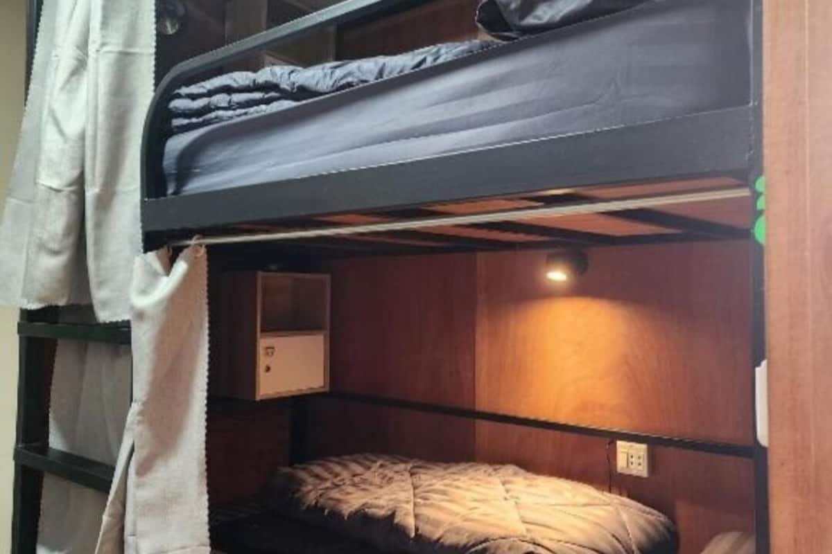 Une chambre avec un lit superposé, une tête de lit en bois, une table de chevet et un rideau suspendu.