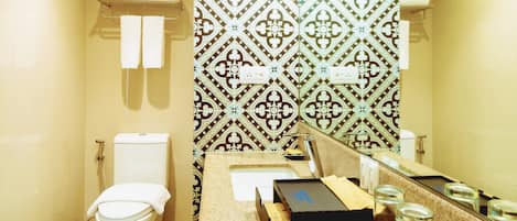 A bathroom with a toilet, towel rack, patterned wall, sink, and toiletries.