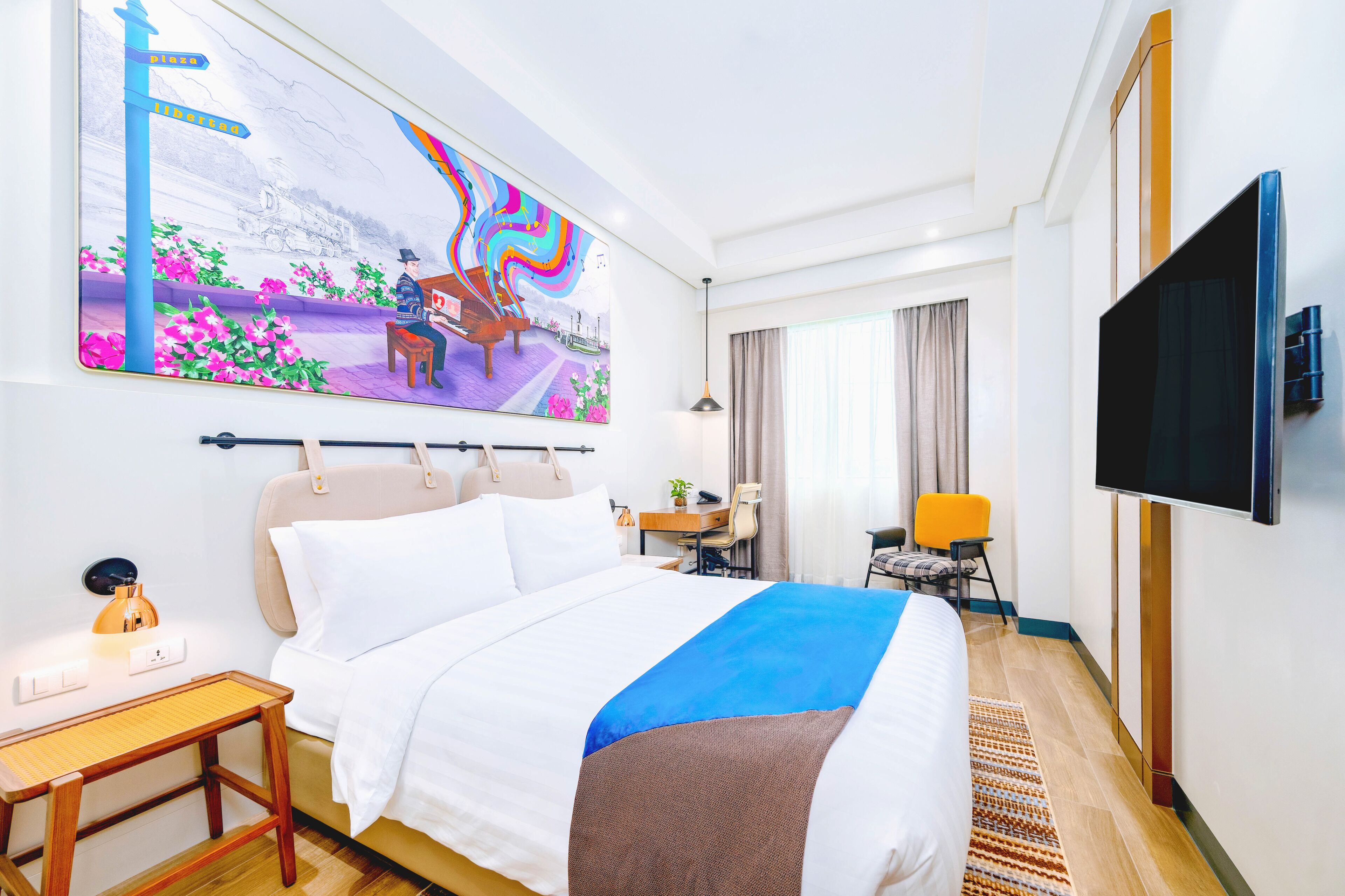 Een hotelkamer met een bed, een bureau, een stoel, een televisie en een schilderij aan de muur.