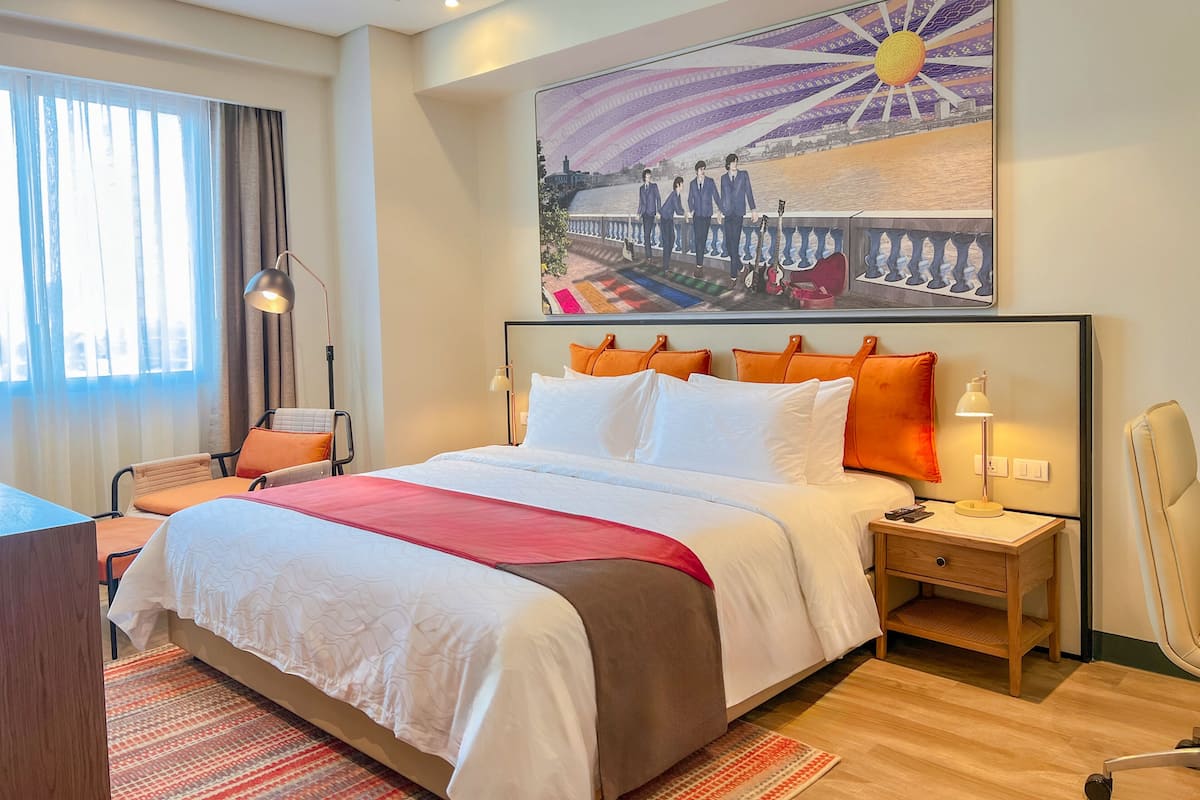 Una camera d'albergo con un letto grande, una scrivania, una sedia, un comodino, una lampada e un grande quadro appeso al muro.