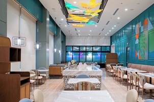 A modern restaurant with a central island, seating around it, and a colorful ceiling design.