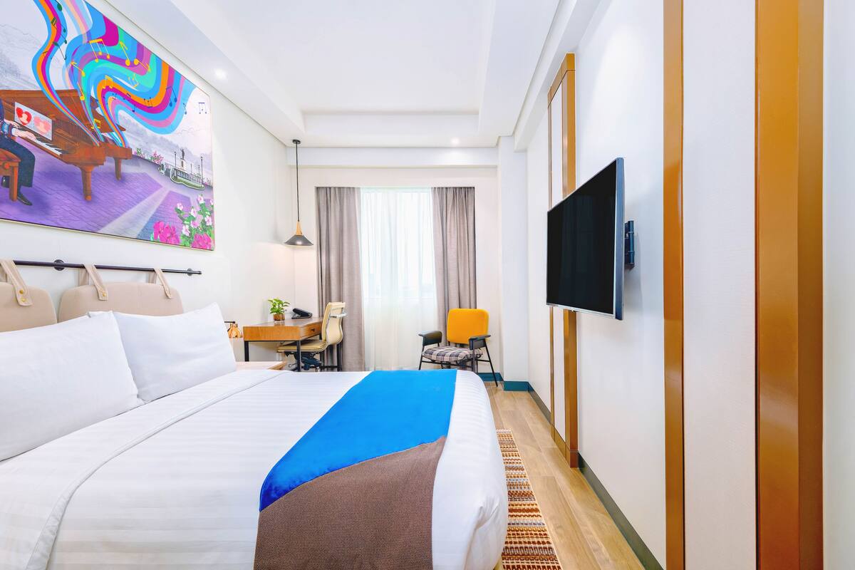 Una camera d'albergo con un letto grande, una scrivania, una sedia, una televisione e un quadro appeso al muro.