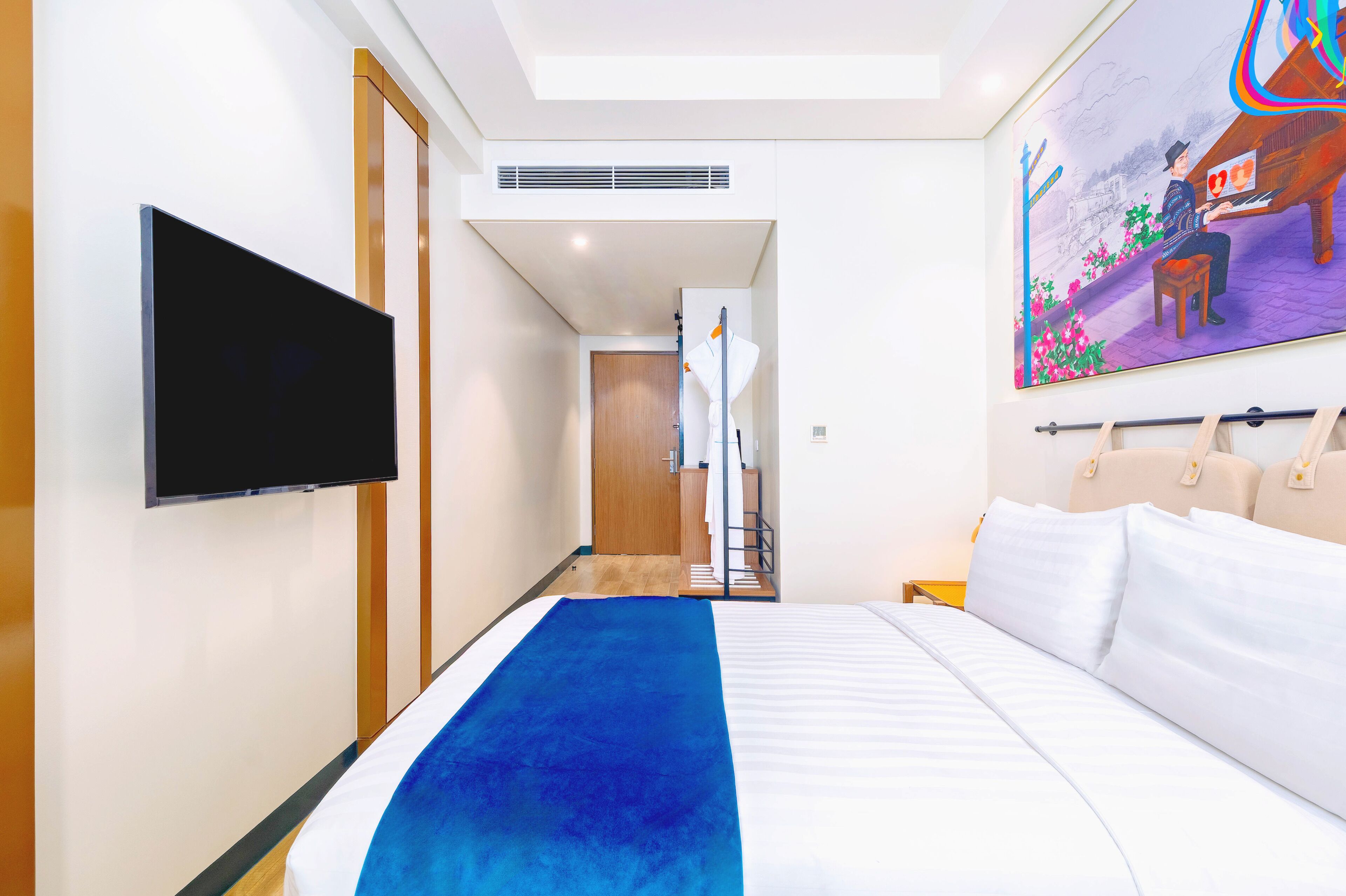 A hotel room with a bed, a flat-screen TV, a painting, and a wooden door.
