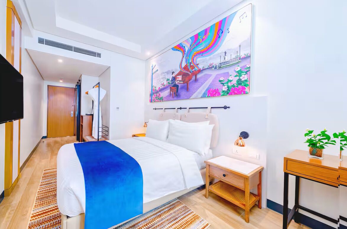 A hotel room with a bed, bedside table, nightstand, and a large wall mural.
