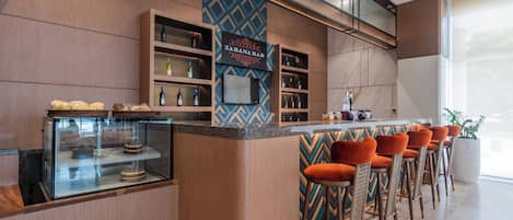 Zona de bar con mostrador, estanterías llenas de botellas y vitrina con pasteles.
