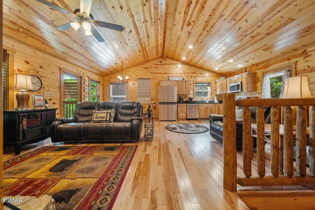 Interior acogedor de una cabaña con sala de estar, cocina y comedor, con paredes y pisos de madera, un sofá de cuero y una mesa de comedor.