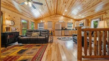 Interior acogedor de una cabaña con sala de estar, cocina y comedor, con paredes y pisos de madera, un sofá de cuero y una mesa de comedor.