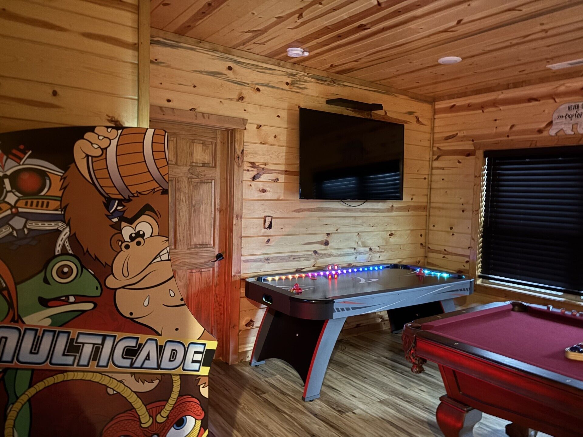 A wooden room with a pool table, a foosball table, and a television mounted on the wall.