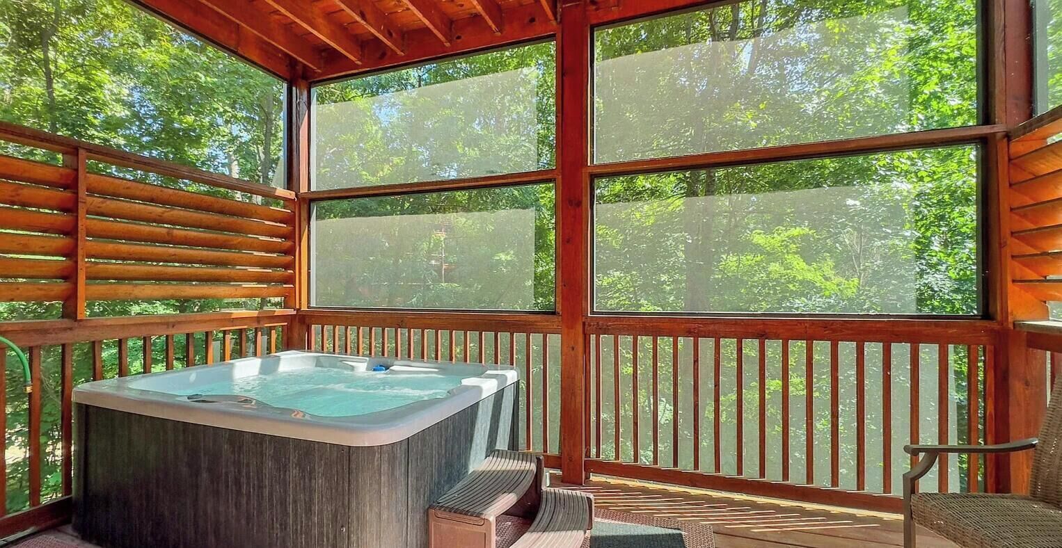 A hot tub on a wooden deck with large windows overlooking a forest.