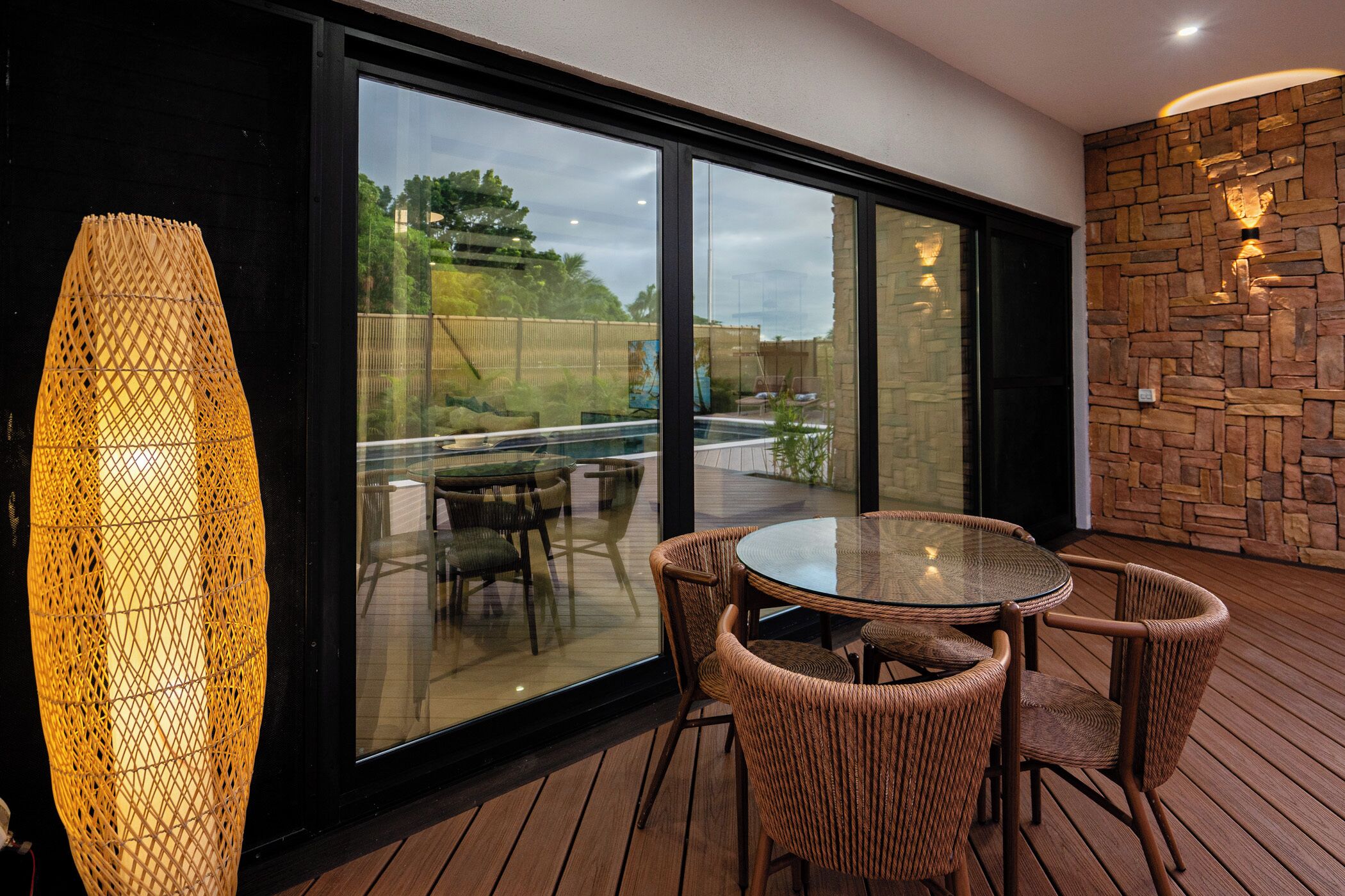 A modern outdoor patio with wicker furniture, a glass table, and a large woven light fixture.