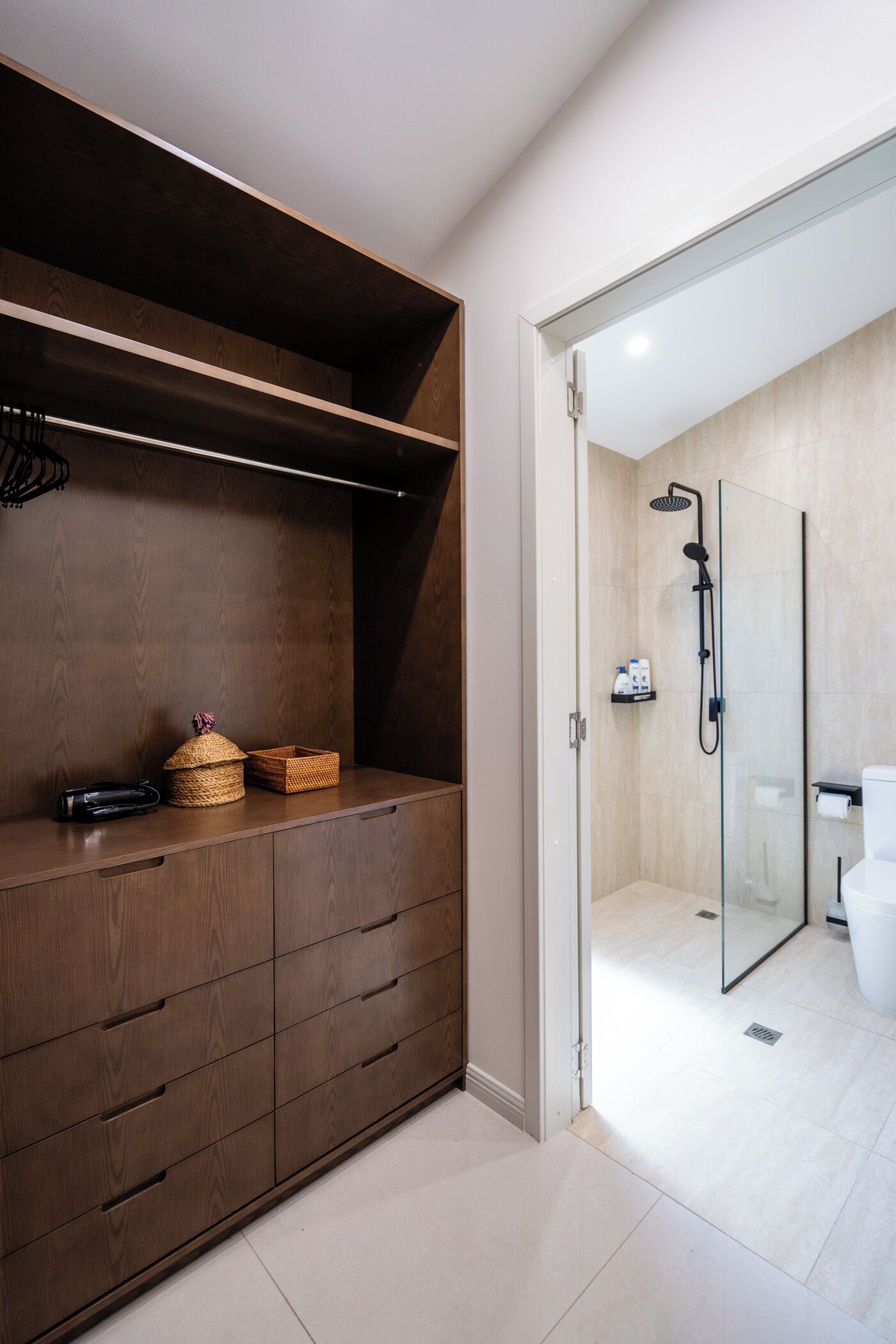 A modern bathroom with a glass shower enclosure, a toilet, and a wooden vanity with drawers and baskets.