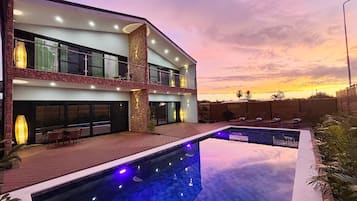 Una moderna casa a due piani con piscina, area salotto esterna e vista sul tramonto.