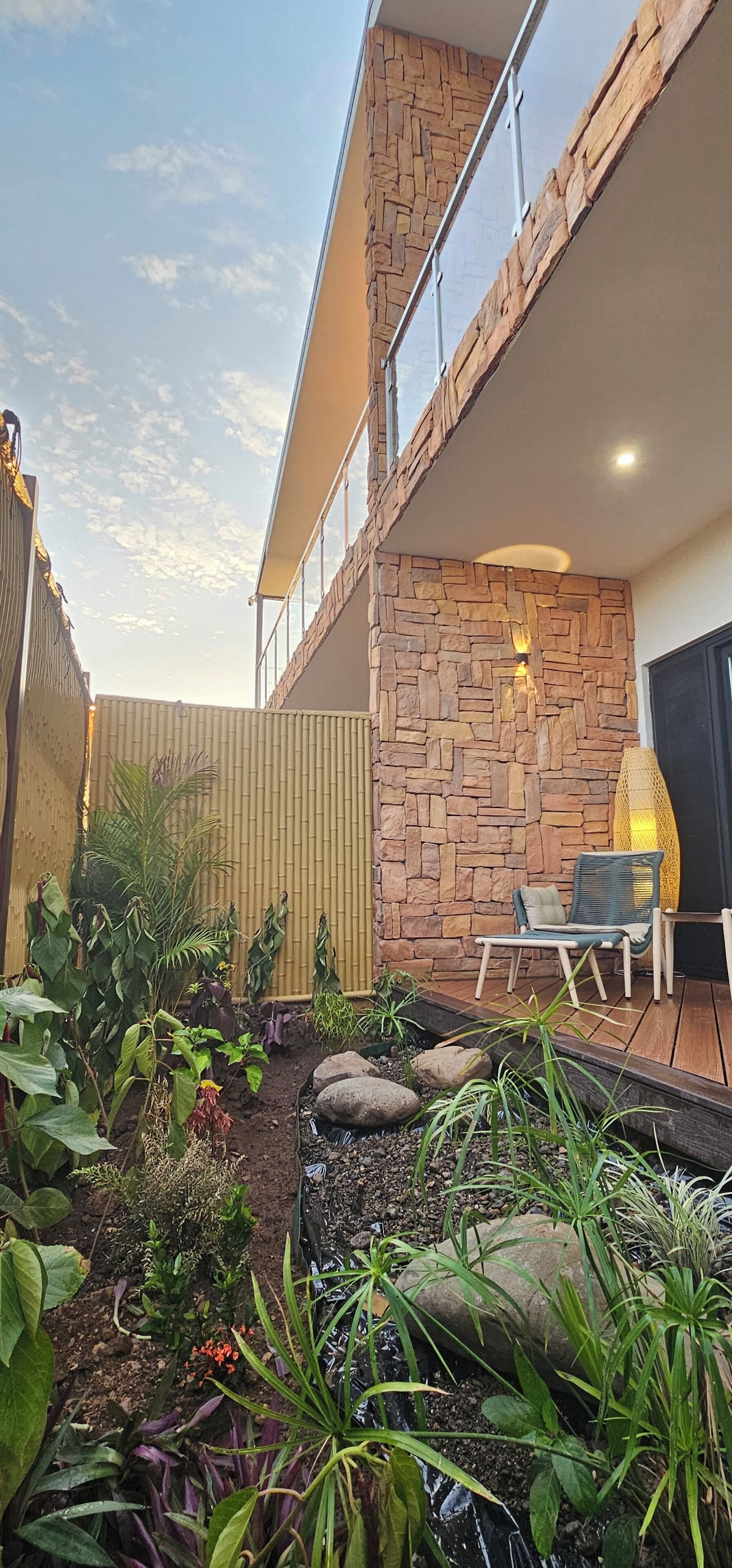 Patio esterno moderno con parete in pietra, un deck in legno e una zona relax con sedia e tavolo.