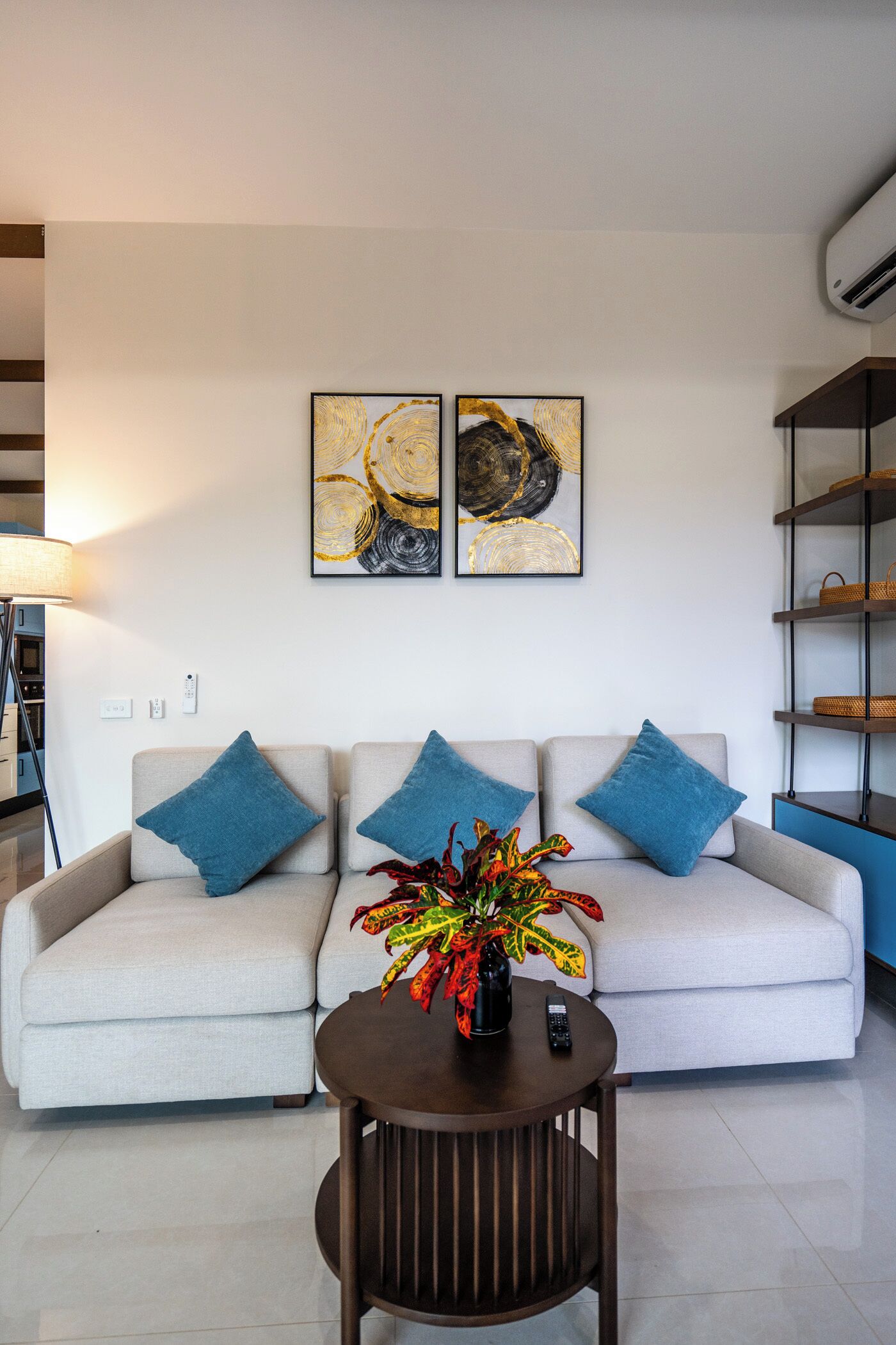 A modern living room with a sofa, blue cushions, a coffee table with a vase of flowers, and two abstract paintings on the wall.