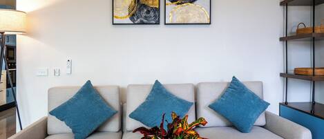 A modern living room with a sofa, blue cushions, a coffee table with a vase of flowers, and two abstract paintings on the wall.