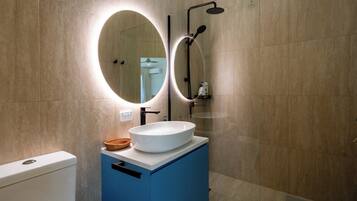 Un baño con un lavamanos blanco, un espejo con luz circular y una zona de ducha.