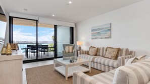 Ett modernt vardagsrum med ett soffbord i glas, en randig soffa och utsikt över havet genom stora skjutdörrar.