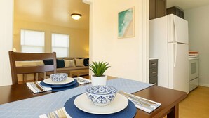 A dining area with a table set for two, a potted plant, and a kitchen in the background. - Mission Beach Stay | A/C • Garage • Steps to Water (San Diego)
