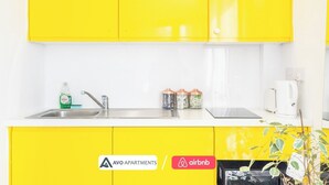 A kitchen with yellow cabinets, a stainless steel sink, and a coffee maker. There are jars on the counter and a plant in the corner. - Chic Studio | Prime Location | Free Parking (Sheffield)