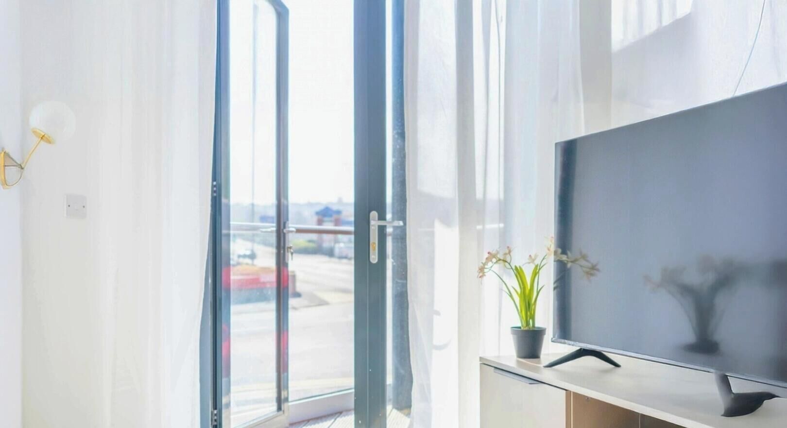 Une chambre moderne dotée d’une grande fenêtre, d’un téléviseur à écran plat et d’une petite plante en pot.