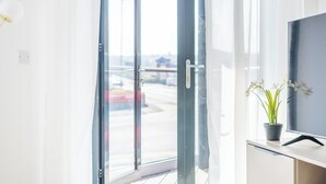 A bright room with a sliding glass door leading to an outdoor area, a flat-screen TV on a cabinet, and a potted plant on the windowsill. - Chic Studio | Prime Location | Free Parking (Sheffield)