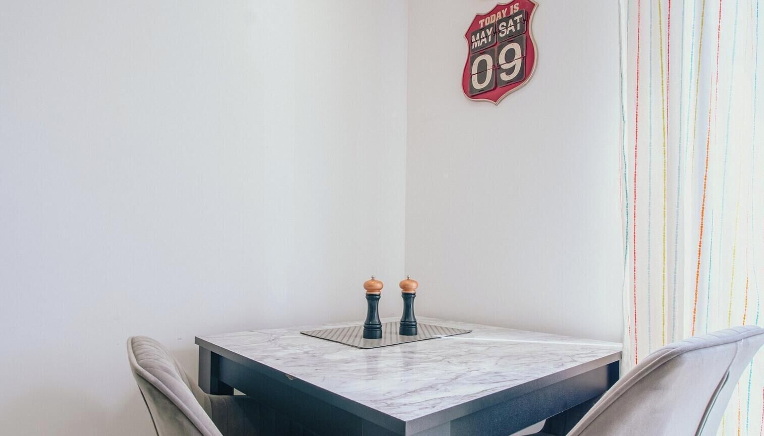 Un pequeño comedor con una mesa de mármol, dos saleros y pimenteros, y un reloj de pared.