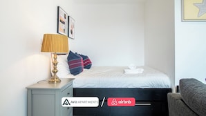 A bedroom with a bed, a bedside table with a lamp, a grey wardrobe, and a framed picture on the wall. - Comfy Studio Apartment in Heart of Sheffield (Sheffield)