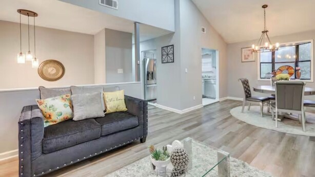 A spacious living area with a dark leather sofa, a glass coffee table, and a dining area with a chandelier.