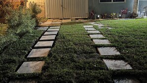 A well-lit backyard with a stone pathway leading to a house, surrounded by greenery and a wooden fence. - Private Chic Studio with Patio • King Bed • Near Beach (Hollywood)