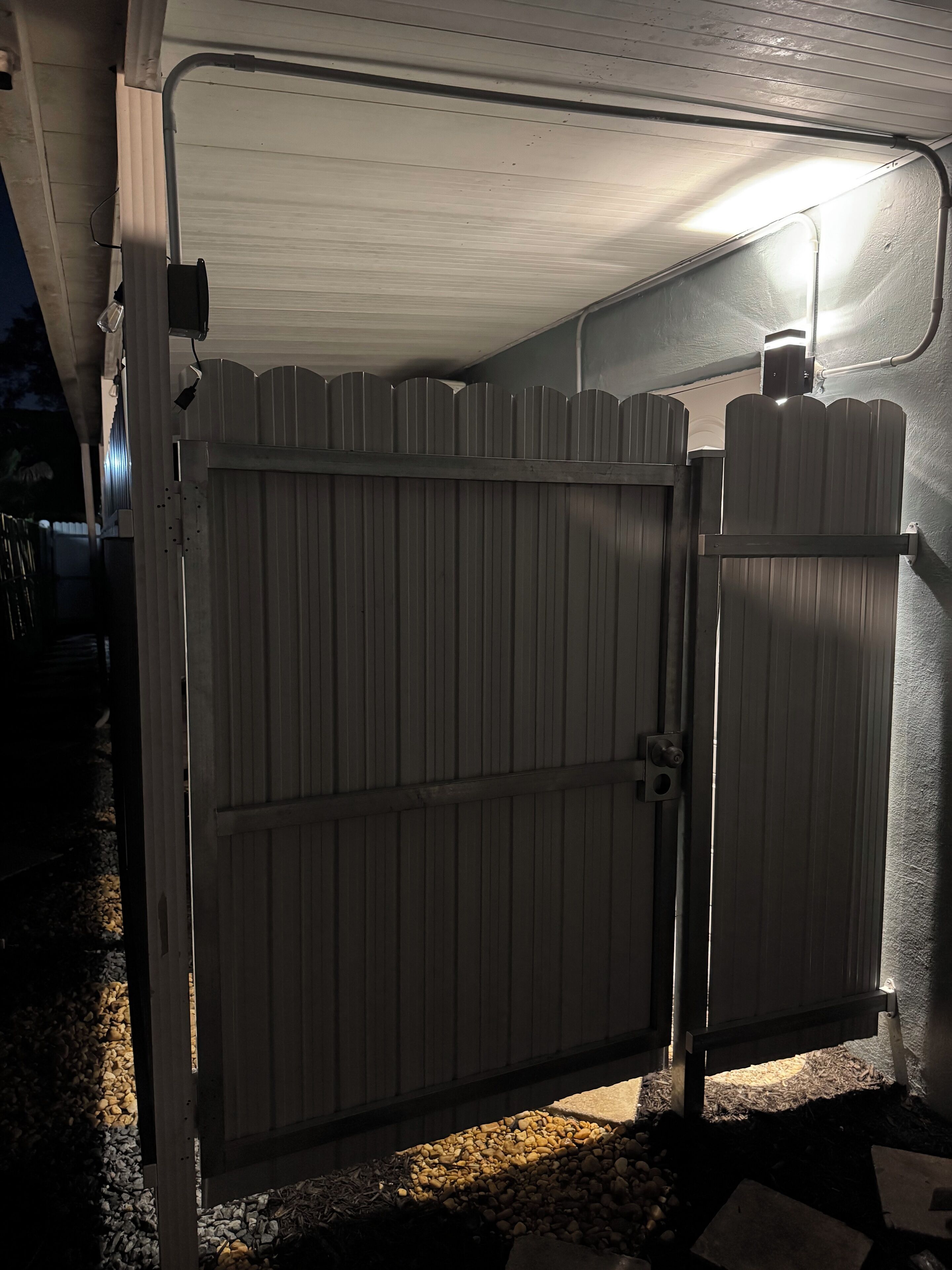 Uma área externa cercada por grades de metal, com piso de concreto e parede branca.