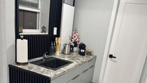 A modern kitchen with a granite countertop, a black and white refrigerator, a sink, and a window with decorative items. - Private Chic Studio with Patio • King Bed • Near Beach (Hollywood)